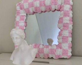 Puede incluir: Un busto de mujer de yeso blanco con un espejo a cuadros rosa y blanco detrás.