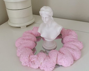 Puede incluir: Un busto de yeso blanco de una mujer con un anillo de espuma rosa alrededor de un espejo.