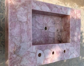 Può includere: Un piano di lavoro per vanità rettangolare in quarzo rosa con un'area lavabo incassata. Il piano di lavoro presenta un motivo a mosaico di pezzi di quarzo rosa e bianco, con tre fori preforati per rubinetti e uno scarico.