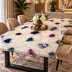 May include: A rectangular dining table featuring a polished white agate stone surface with embedded purple, blue, and teal gemstone slices. The table is supported by a black metal frame and is surrounded by eight beige upholstered chairs.