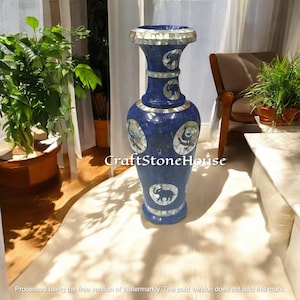 Puede incluir: Un jarrón decorativo azul alto con diseños de elefantes y flores. El jarrón está hecho de un mosaico de piedras azules y blancas. El jarrón tiene una base ancha y una parte superior acampanada. El texto "CraftStoneHouse" es visible en el jarrón.