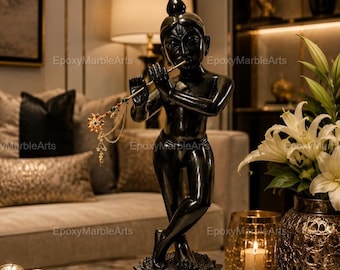 Puede incluir: Una estatua negra brillante de una figura sobre una base de loto, tocando una flauta dorada fina adornada con pequeñas cuentas de colores y cadenas colgantes. La figura tiene un acabado oscuro y liso, y se muestra en una pose con piernas cruzadas.