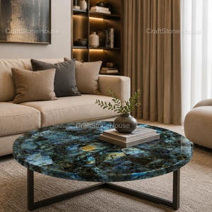 May include: A round coffee table with a striking blue and green stone top, set on a black metal frame. The table is the focal point of a living room, complemented by a beige sofa and armchair. A vase with greenery sits on the table.