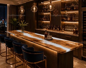 May include: A long bar counter featuring a natural wood slab with a central white resin river design, illuminated by under-counter lighting. Four dark blue velvet bar stools with gold metal frames are positioned along the front of the bar.