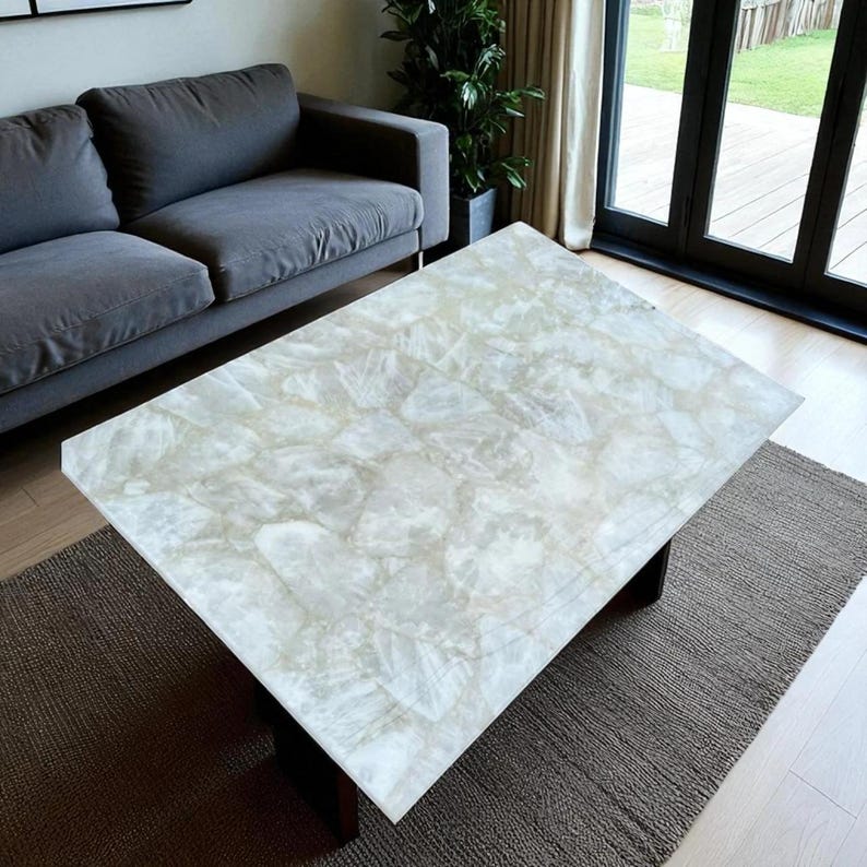 May include: A rectangular coffee table with a light-colored, patterned top. The top appears to be made of a translucent material with a mosaic-like design. The table has dark legs and sits on a neutral-colored rug.