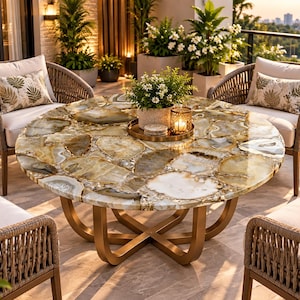 May include: A round table featuring a surface made of polished, multi-colored agate slices in shades of amber, cream, and gray, supported by a gold-toned metal base with a cross-leg design, surrounded by four woven chairs with white cushions.
