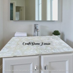 May include: A white marble countertop with a light pattern, installed over a white cabinet. A chrome faucet and a small potted plant are visible. The text "Craft Stone House" is displayed on the countertop.