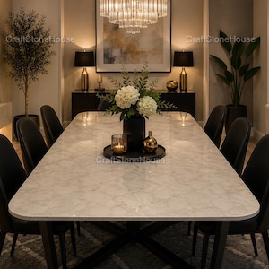 Puede incluir: Comedor moderno con una gran mesa con tapa de mármol, rodeada de sillas negras. Un jarrón negro con flores blancas se encuentra sobre la mesa, junto con una vela y objetos decorativos. Una lámpara de araña cuelga encima.
