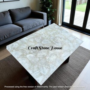 May include: A rectangular coffee table with a light-colored, patterned stone top. The table has a dark base and sits on a neutral-colored rug. The text "Craft Stone House" is visible on the table's surface.
