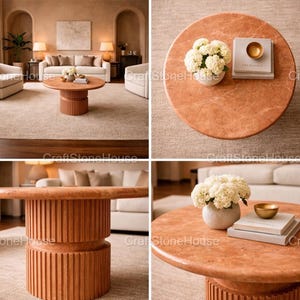 May include: A circular, terracotta-hued coffee table with a ribbed base. The tabletop features a vase of white flowers, books, and a small gold bowl. The table is a focal point in a living room.