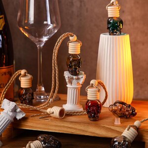 Puede incluir: Un conjunto de seis botellas de vidrio con forma de calavera con tapones de madera y cordones de cuerda. Las botellas están llenas de un líquido oscuro y cuelgan de un pilar blanco. Las botellas están sobre una superficie de madera.