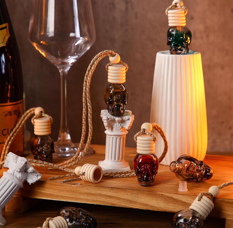 May include: A set of six skull-shaped glass bottles with wooden stoppers and rope cords. The bottles are filled with a dark liquid and are hanging from a white pillar. The bottles are on a wooden surface.