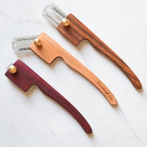 May include: Three wooden straight razors with a metal blade and a brass knob. The razors are made of different types of wood, including maple, walnut, and purpleheart. The razors are engraved with the words "Sourdough Era" and "Shaverb".