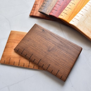 May include: A set of five wooden cutting boards with a ruler etched on the surface. The boards are made of different types of wood, including maple, walnut, and cherry. The boards are all approximately 12 inches long and 6 inches wide.