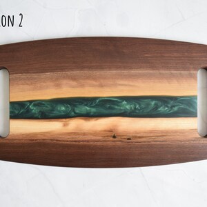 Op de afbeelding: Een houten serveerschaal met twee handvatten. De schaal heeft een groene epoxyhars inlay en een natuurlijke houtkleur.  OPTION 2 staat in zwarte tekst in de linkerbovenhoek van de schaal.