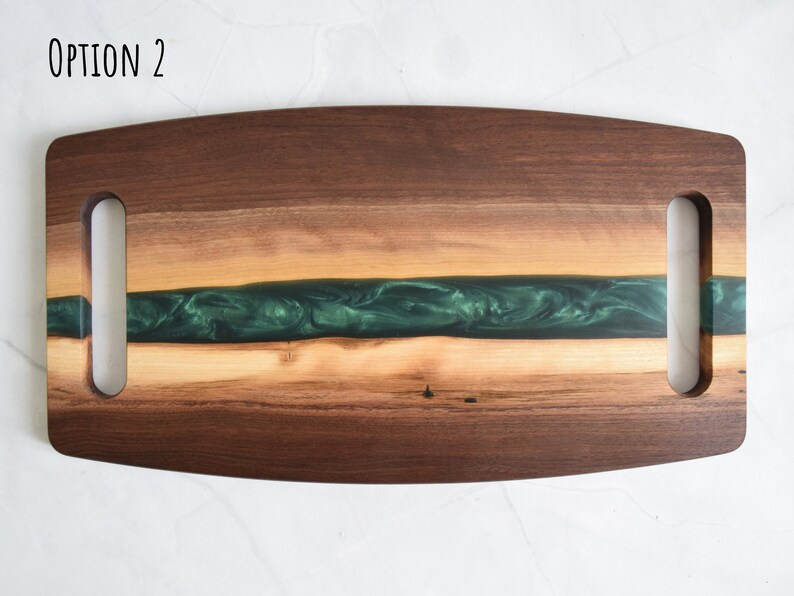 Op de afbeelding: Een houten serveerschaal met twee handvatten. De schaal heeft een groene epoxyhars inlay en een natuurlijke houtkleur.  OPTION 2 staat in zwarte tekst in de linkerbovenhoek van de schaal.