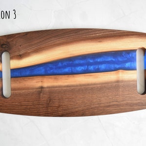 Op de afbeelding: Een houten serveerschaal met twee handvatten. De schaal heeft een blauwe harsinleg die lijkt op een rivier.