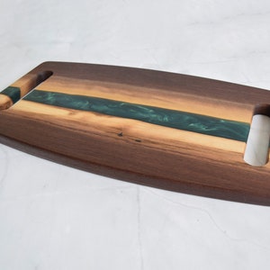 Op de afbeelding: Een houten serveerschaal met twee handvatten. De schaal is gemaakt van walnoot hout en heeft een inleg van groene epoxyhars.