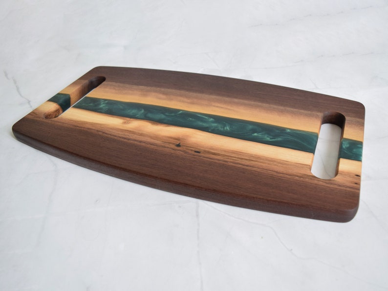 Op de afbeelding: Een houten serveerschaal met twee handvatten. De schaal is gemaakt van walnoot hout en heeft een inleg van groene epoxyhars.