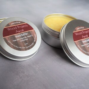 May include: Two silver tins of wood butter, each with a red and brown label that reads "Wood Projects Await" and "Wood Butter". The label also says "Made with mineral oil, vitamin E and beeswax" and "Buff onto surface with cloth - Leave overnight - Wipe off excess".