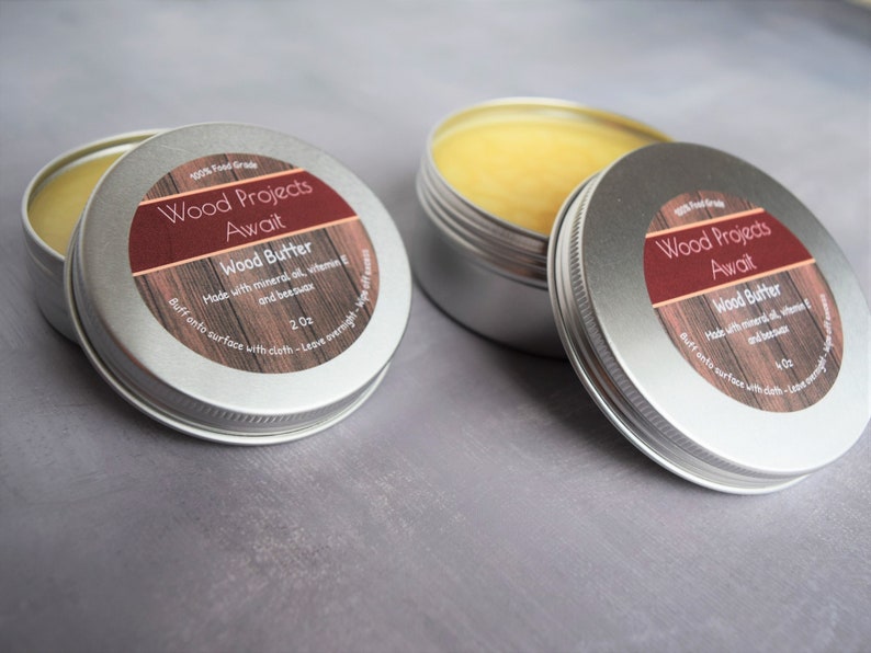 May include: Two silver tins of wood butter, each with a red and brown label that reads "Wood Projects Await" and "Wood Butter". The label also says "Made with mineral oil, vitamin E and beeswax" and "Buff onto surface with cloth - Leave overnight - Wipe off excess".
