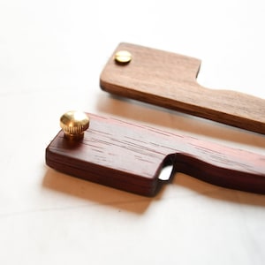 May include: Two wooden tools with brass accents. One tool is a dark red wood with a brass knob and a small blade. The other tool is a light brown wood with a brass screw.