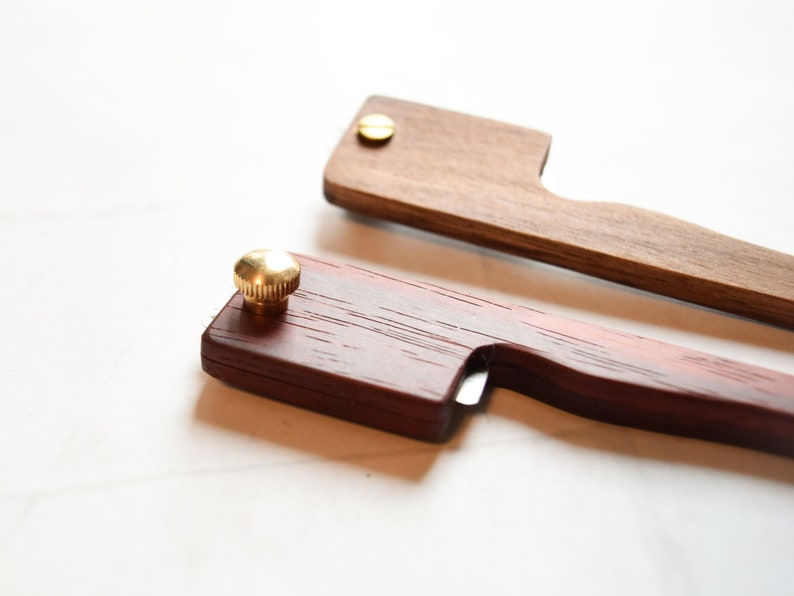 May include: Two wooden tools with brass accents. One tool is a dark red wood with a brass knob and a small blade. The other tool is a light brown wood with a brass screw.