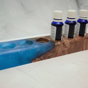 May include: A wooden essential oil holder with three blue glass bottles and three blue resin wells. The holder has a natural wood grain finish.