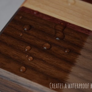 May include: Close-up of a wooden chopping board with a dark brown finish. Water droplets bead on the surface, demonstrating the waterproof barrier created by the finish.