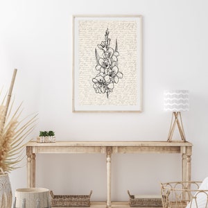 May include: A black and white line drawing of a flower bouquet on a cream background with a handwritten script pattern. The drawing is framed and hanging on a white wall above a wooden console table with a wooden sign that says "HOME".