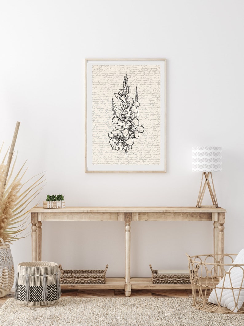 May include: A black and white line drawing of a flower bouquet on a cream background with a handwritten script pattern. The drawing is framed and hanging on a white wall above a wooden console table with a wooden sign that says "HOME".