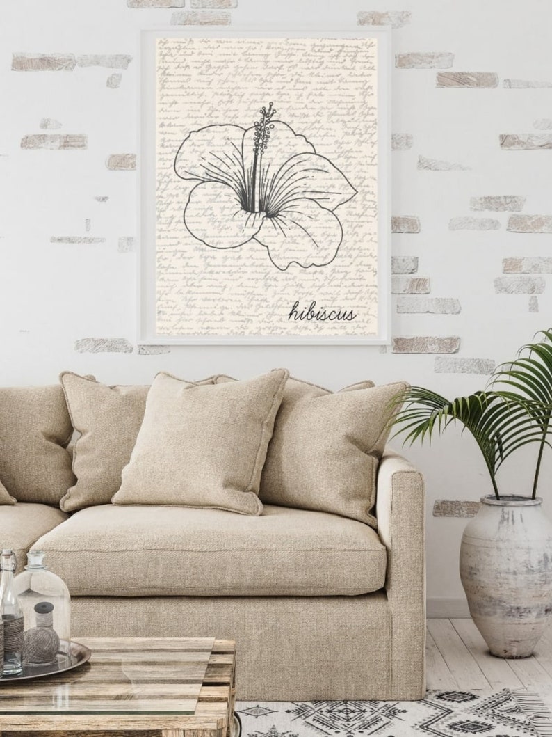 Puede incluir: Una impresi&oacute;n art&iacute;stica enmarcada con una ilustraci&oacute;n en blanco y negro de una flor de hibisco. La obra de arte est&aacute; sobre un fondo de escritura a mano. La palabra "hibiscus" est&aacute; escrita en cursiva. La impresi&oacute;n se muestra sobre un sof&aacute; beige.