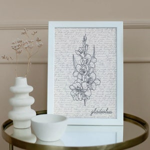 May include: A white framed print with a black and white line drawing of a gladiolus flower on a background of handwritten text. The text at the bottom of the print reads "gladiolus".