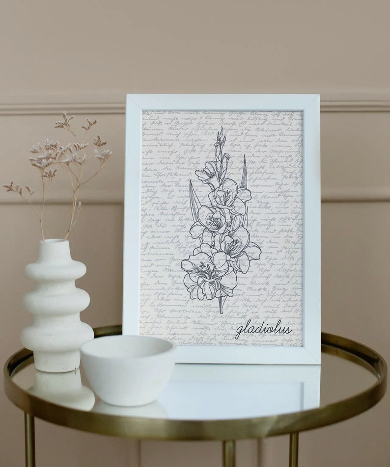 May include: A white framed print with a black and white line drawing of a gladiolus flower on a background of handwritten text. The text at the bottom of the print reads "gladiolus".