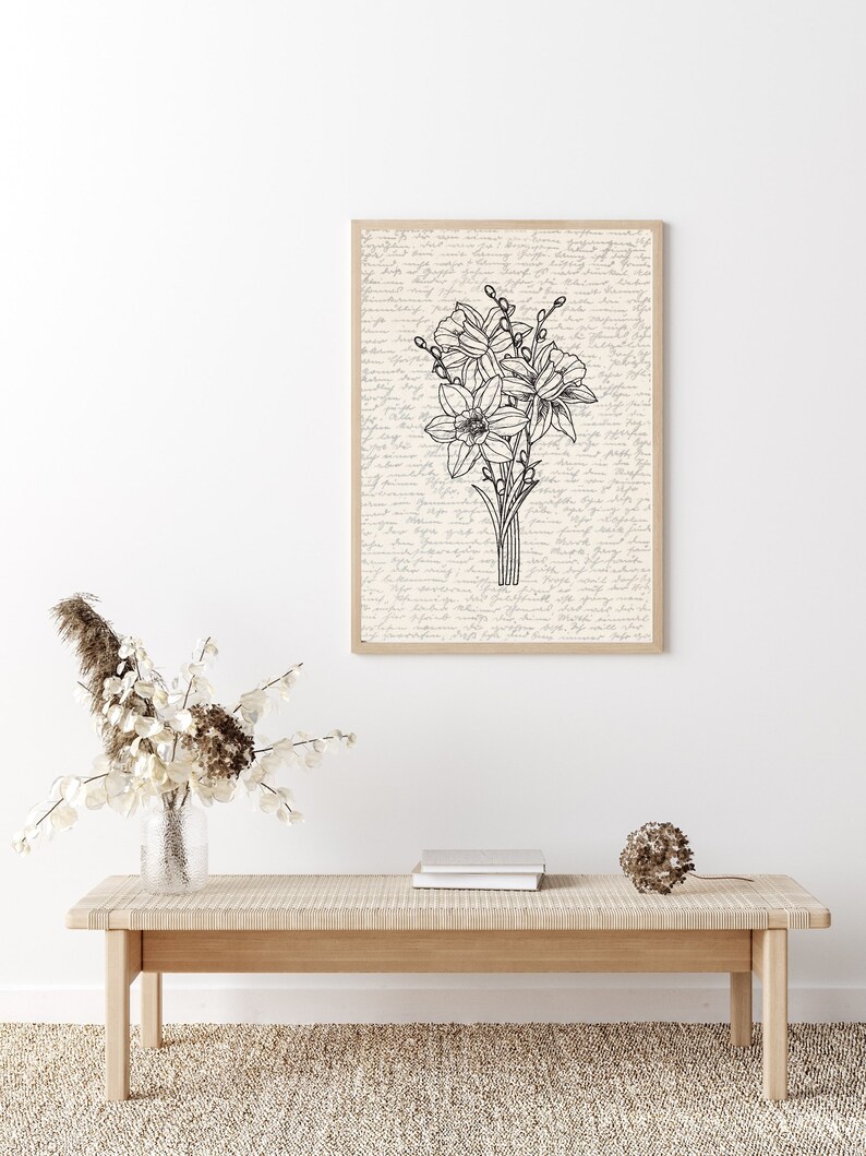 May include: A black and white line drawing of a bouquet of daffodils on a cream background with handwritten text. The drawing is framed in a light wood frame.