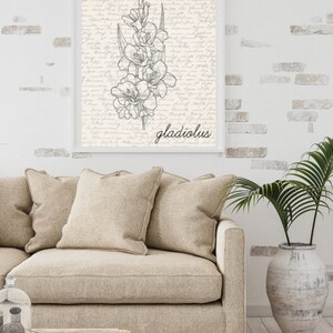 May include: A black and white line drawing of a gladiolus flower on a cream background with a handwritten script pattern. The word "gladiolus" is written in black below the flower.
