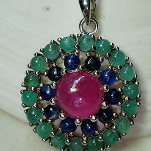 May include: A silver necklace with a round pendant featuring a large pink ruby surrounded by smaller green emeralds and blue sapphires.