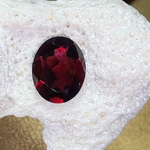 May include: A deep red gemstone with a faceted cut, set against a white background.