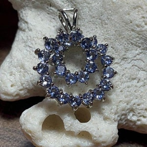 Puede incluir: Un colgante de plata con un diseño de doble círculo con un grupo de piedras preciosas de color azul claro.