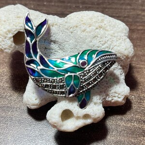 May include: A silver whale brooch with green, blue, and purple enamel and marcasite accents.