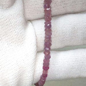 Puede incluir: Una hebra de cuentas de piedras preciosas rosadas. Las cuentas son facetadas y tienen una forma ligeramente irregular. Las cuentas están enhebradas en un hilo transparente.