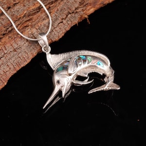 May include: A silver marlin pendant necklace with iridescent abalone shell inlay. The marlin is depicted leaping out of the water with its dorsal fin extended. The necklace is on a silver chain.