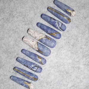 Puede incluir: Conjunto de diez u&ntilde;as postizas largas de color azul, de imitaci&oacute;n de mezclilla, con detalles de encaje blanco y cierre dorado.