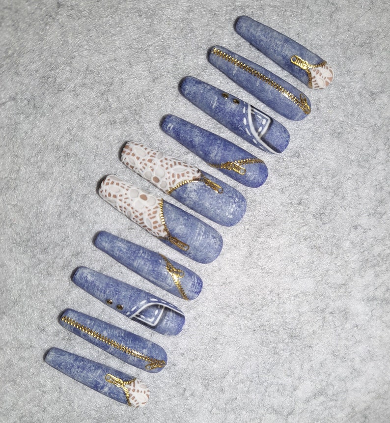 Puede incluir: Conjunto de diez u&ntilde;as postizas largas de color azul, de imitaci&oacute;n de mezclilla, con detalles de encaje blanco y cierre dorado.