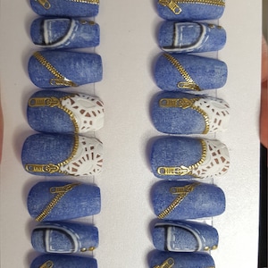 Puede incluir: Conjunto de diez u&ntilde;as postizas azules y blancas con detalles de cremallera dorada. Las u&ntilde;as est&aacute;n decoradas con un patr&oacute;n de mezclilla y encaje blanco.