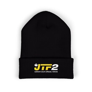 Può includere: Berretto nero con bordo ripiegato. La parte anteriore presenta la scritta "JTF2" in giallo e bianco, con una grafica a foglia d'acero e la scritta "CANADA'S ELITE SPECIAL FORCES" in bianco.