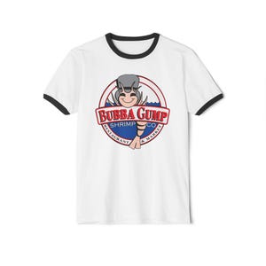 以下が含まれることがあります： 襟と袖に黒いトリムが付いた白いTシャツ。シャツには、「BUBBA GUMP SHRIMP CO. RESTAURANT & MARKET」というテキストと漫画のエビのキャラクターが描かれた円形のロゴが付いています。