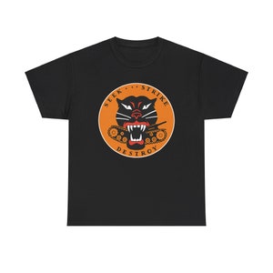 Puede incluir: Camiseta negra con un gráfico circular naranja que presenta un pantera negra con un tanque en su boca. El texto "SEEK...STRIKE...DESTROY" está escrito alrededor del círculo.