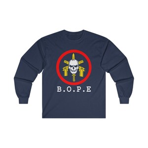 May include: Navy blue long-sleeve shirt featuring a circular emblem with a skull, guns, and a knife, surrounded by a red ring. The text "B.O.P.E" is printed in white below the emblem. The shirt is made of a soft material.