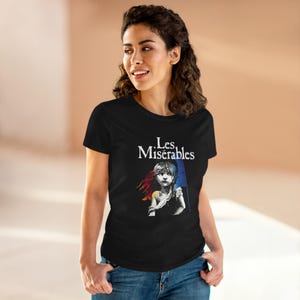 Pode incluir: T-shirt preto com o texto "Les Misérables" em branco sobre um gráfico de uma menina com uma bandeira. O gráfico inclui cores vermelha, amarela e azul.